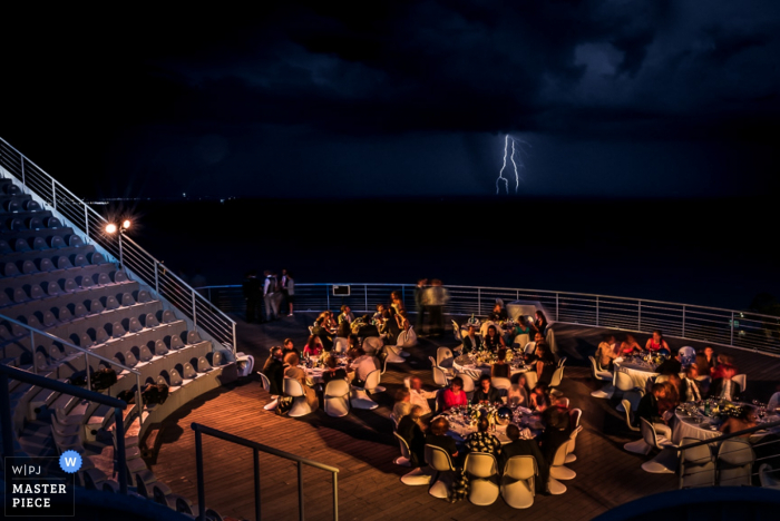 Photo: <a href="https://www.wpja.com/contests/2016-q3-photography-contest/weather/1915706"> Benjamin Brette - France </a> Photo des invités assis dehors la nuit lors de la réception sous les éclairs d'un photographe de mariage en France.
