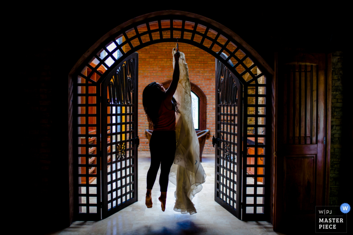 Photo by: <a href="https://www.wpja.com/contests/2016-q3-photography-contest/getting-ready/1895726">Ben Chrisman - United States</a> Photo of a woman jumping in the air to hang the bride's gown above a doorway by a Charleston, SC wedding photographer.