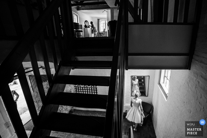 Photo by: <a href="https://www.wpja.com/contests/2016-q3-photography-contest/getting-ready/1905481">Anton Podolskiy - Germany</a> Black and white photo of the bride checking herself in a mirror downstairs as another woman gets ready upstairs by a Lower Saxony, Germany wedding photographer.