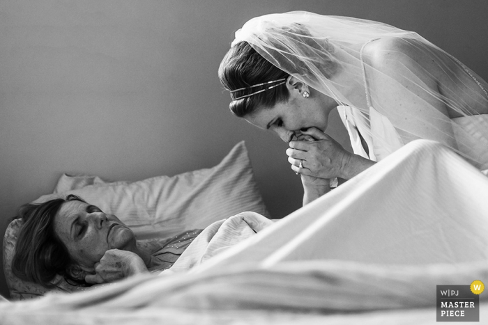 Black and white photo of the bride kissing a woman's hand as she lays in bed by a San Francisco, CA wedding photographer.