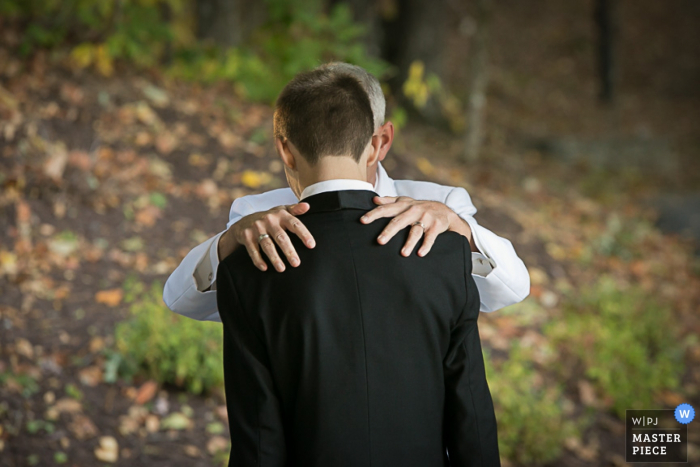 Von einem Hochzeitsfotografen aus Atlanta, GA, aufgenommenes Rückfoto eines Mannes, der seine Hände auf die Schultern des Bräutigams legt.