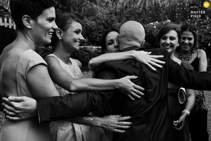 Foto em preto e branco de um grupo de mulheres abraçando um homem, tirada por um fotógrafo de casamento em Madri, Espanha.