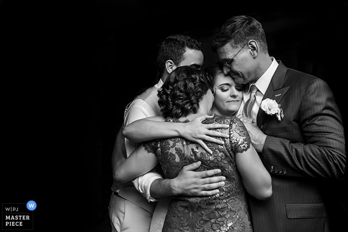 Black and white photo of the bride and groom in a group hug with guests by a Washington, D.C. wedding photographer.