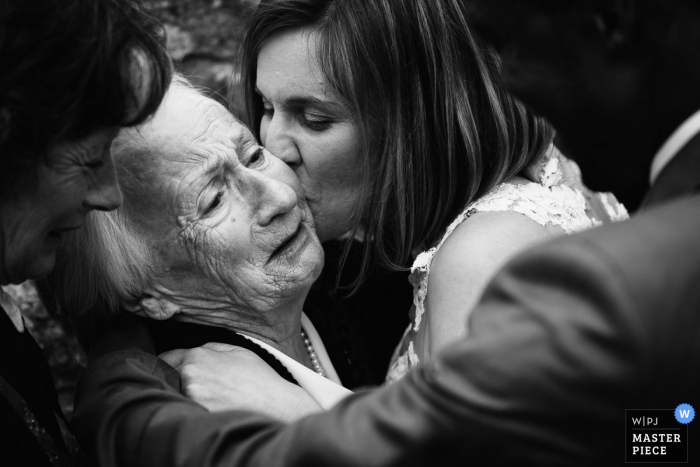 Foto em preto e branco da noiva beijando uma mulher na bochecha, feita por um fotógrafo de casamento em Playas de la Loire, França.