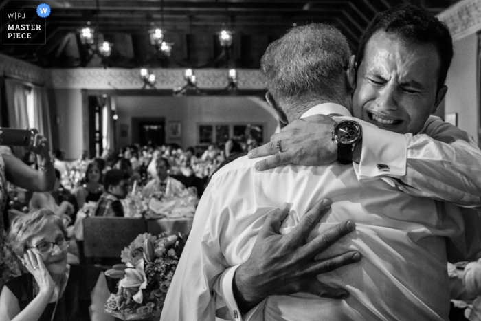 Black and white photo of the groom hugging an older man during the reception by an Alicante, Valencia wedding photographer.