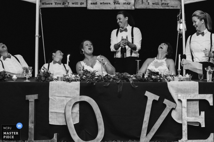 Foto por: <a href="https://www.wpja.com/contests/2016-q4-photography-competition/toastingspeeches/1933921"> Leah Moyers - Estados Unidos </a> Foto en blanco y negro de la novia y los invitados riendo durante un discurso de un fotógrafo de bodas en Knoxville, TN.