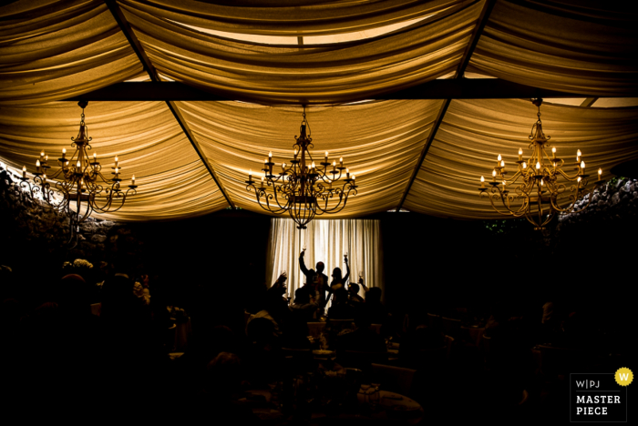 Photo by: <a href="https://www.wpja.com/contests/2016-q4-photography-competition/toastingspeeches/1954871">Stefano Serra - Italy</a> Photo of guests silhouetted while giving a toast in a tent beneath large chandeliers by a Turin, Italy wedding photographer.