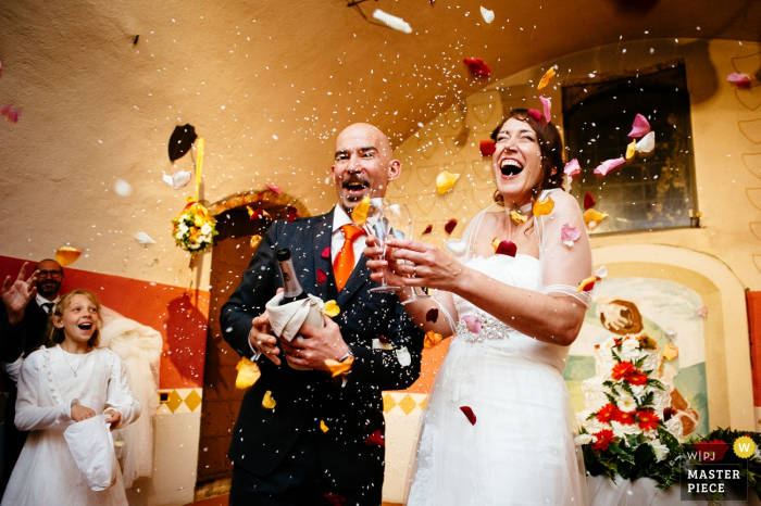 Photo by: <a href="https://www.wpja.com/contests/2016-q4-photography-competition/toastingspeeches/1958796">Alessandro Avenali - Italy</a> The bride and groom hold champagne and two glasses as guests toss rice and flower petals in this photo by a Rome wedding photographer.