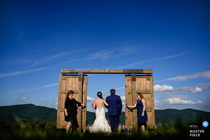 Photo by: <a href="https://www.wpja.com/contests/2016-q4-photography-competition/symmetry/1950486">Jacob Hannah - United States</a> The bride and groom walk through a doorway in an open field in this photo by a Burlington, VT wedding photographer.