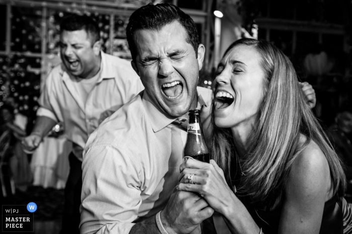 Photo by: <a href="https://www.wpja.com/contests/2016-q4-photography-competition/symmetry/1960661">Danette Pascarella - United States</a> Black and white photo of two guests singing as they pretend to use a bottle as a microphone by a New Jersey wedding photographer.