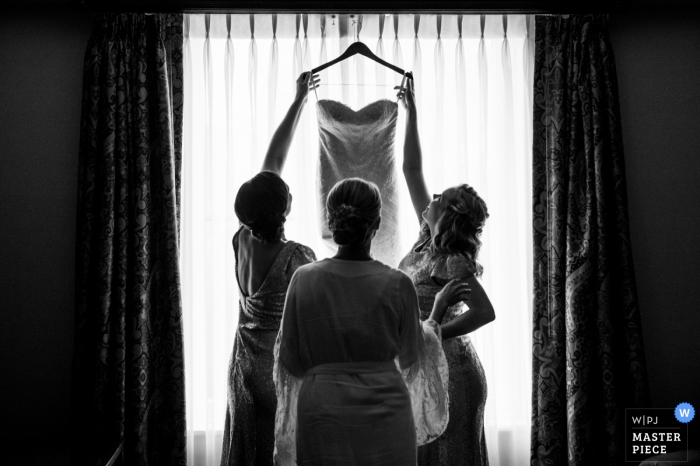 Photo by: <a href="https://www.wpja.com/contests/2016-q4-photography-competition/symmetry/1979066">Morgan Lynn Razi - United States</a> Black and white photo of two bridesmaids preparing to help the bride into her wedding gown by a Houston, TX wedding photographer.