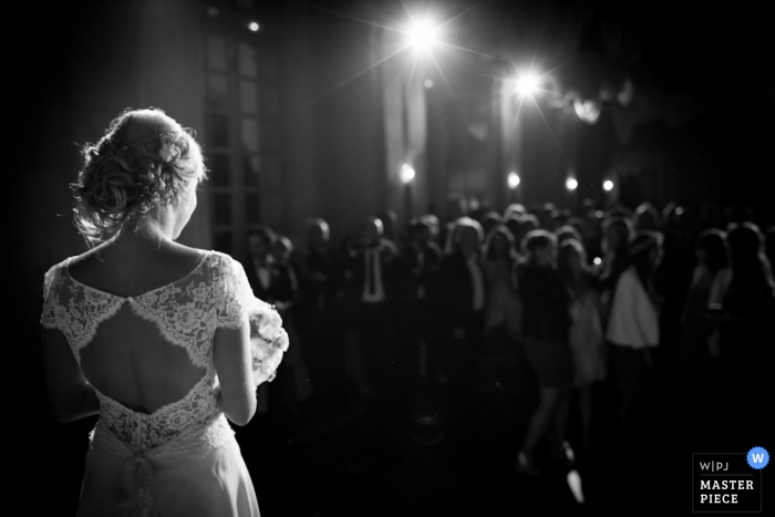 Black and white photo of the bride standing in front of her guests with lights beaming overhead by a Paris, France wedding photographer.