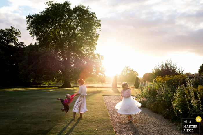 Três crianças brincam no jardim iluminado pelo sol nesta foto de um fotógrafo de reportagens de casamento em Londres, Inglaterra.