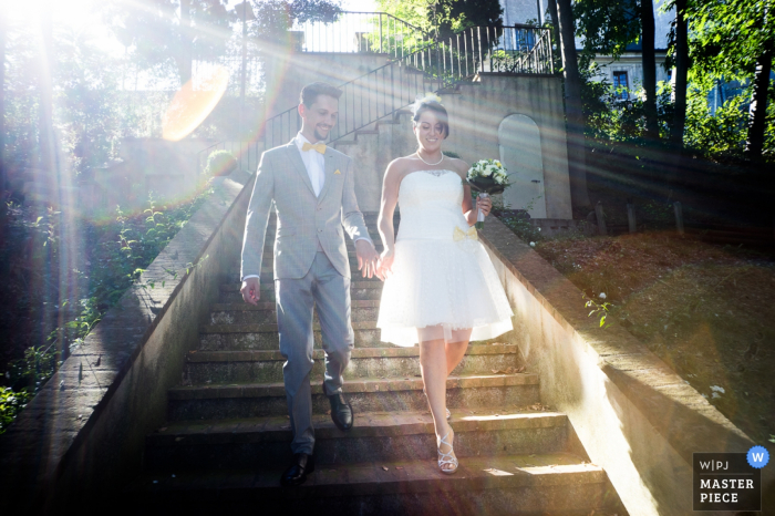 Foto por: <a href="https://www.wpja.com/contests/2016-q4-photography-competition/lens-flare-refraction/1934626"> Alessandro Di Noia - Italia </a> Los novios caminan por un tramo de escaleras afuera mientras los rayos del sol brillan sobre ellos en esta foto de un fotógrafo de bodas de Lombardía.