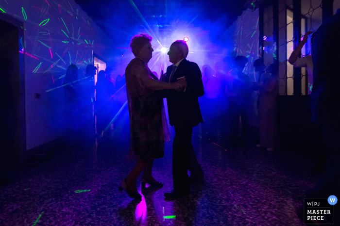 Una pareja de más edad baila en la pista de baile con luz azul en esta foto de un fotógrafo de bodas de Venecia.