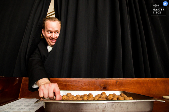 Photo by: <a href="https://www.wpja.com/contests/2016-q4-photography-competition/humor/1960606">Danette Pascarella - United States</a> A guest reaches around a black curtain to sneak a bit of food in this photo by a New Jersey wedding photographer.
