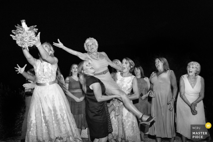 Photo by: <a href="https://www.wpja.com/contests/2016-q4-photography-competition/bouquetgarter-action/1945391">Fabio Mirulla - Italy</a> A woman is lifted by two others as she and another guest try to catch the bouquet in this black and white photo by a Tuscany wedding photographer.
