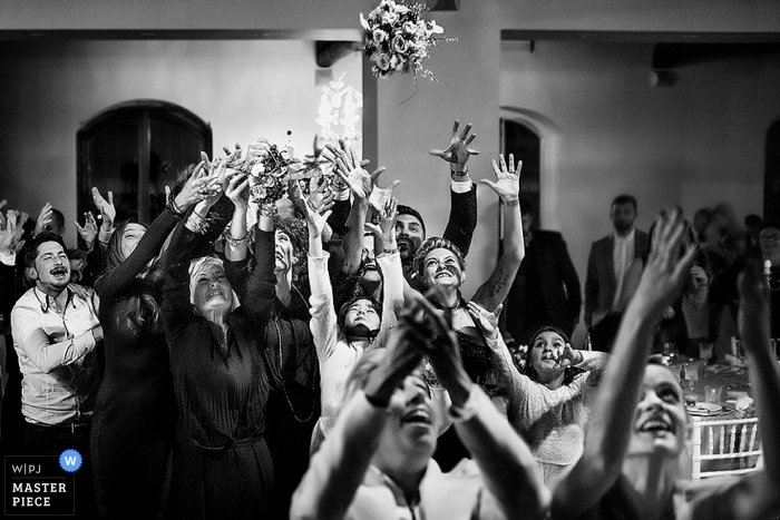 Black and white photo of guests reaching up to catch the bride's bouquet by a Tuscany wedding photographer.