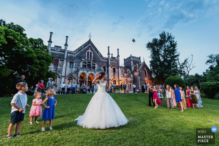 A noiva joga seu buquê em um gramado grande em frente a um edifício imponente nesta foto por um fotógrafo de casamento de Veneza.