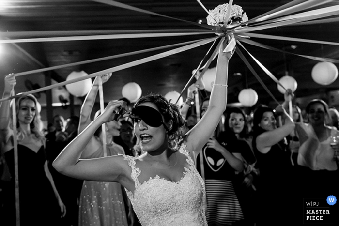 Photo by: <a href="https://www.wpja.com/contests/2016-q4-photography-competition/bouquetgarter-action/1957936">Leandro Donato - Brazil</a> Black and white photo of the bride lifting her blindfold as the women around her carry ribbons tied to her bouquet by a Brazil wedding photographer.