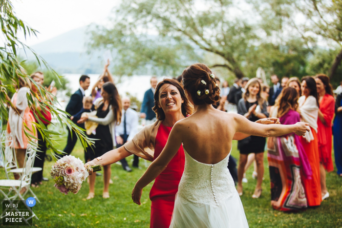 Die Braut und ein Gast, die den Blumenstrauß tragen, nähern sich einander für eine Umarmung in diesem Foto von einem Hochzeitsfotografen in Umbrien, Italien.