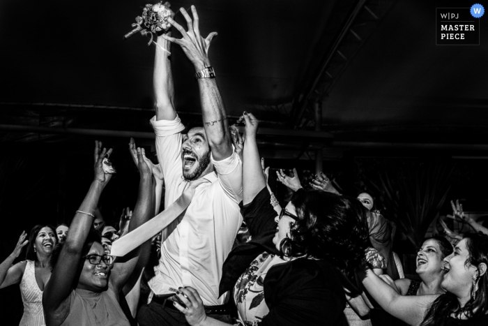 Black and white photo of guests reacting excitedly during the bouquet and garter toss portion of the reception by a Rio de Janeiro, Brazil wedding photographer.