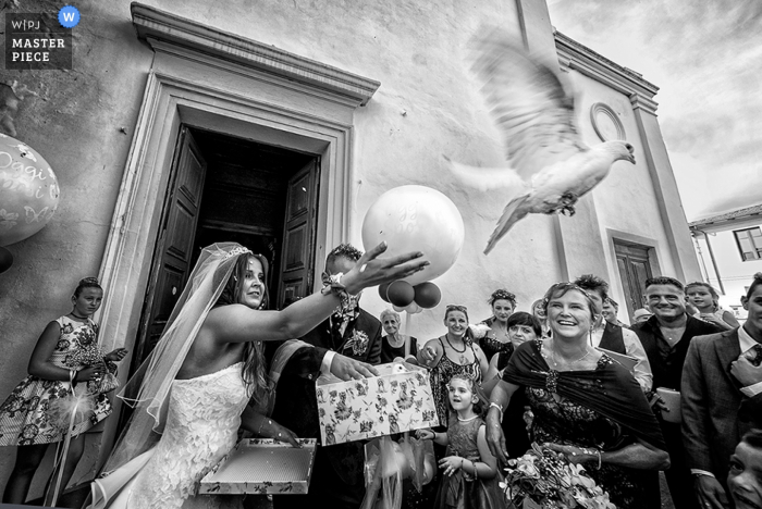 Zdjęcie: <a href="https://www.wpja.com/contests/2016-q4-photography-competition/ceremony/1941666"> Alessandro Colle - Włochy </a> Po ceremonii panna młoda wypuszcza białą gołębicę, gdy goście oglądają to czarno-białe zdjęcie autorstwa toskańskiego fotografa ślubnego.