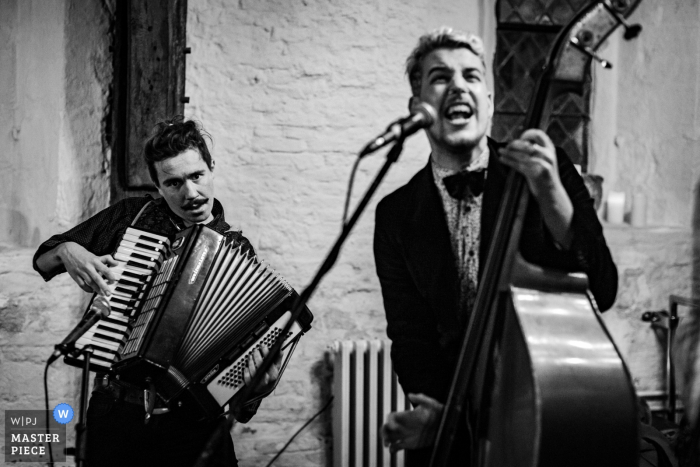 Foto door: <a href="https://www.wpja.com/contests/2016-q4-photography-competition/musicians-djs/1940996"> Alex Abbott - Verenigd Koninkrijk </a> Zwart-witfoto van de bassist en accordeonist die tijdens de ontvangst door een fotograaf van de de huwelijksreportage van West-Yorkshire, Engeland speelt.