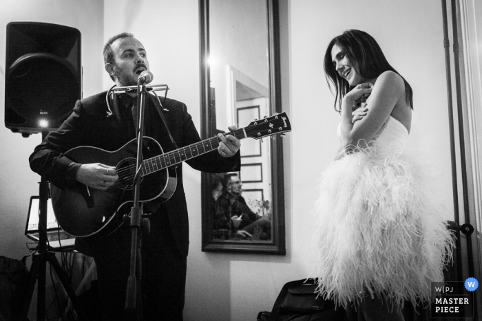Foto door: <a href="https://www.wpja.com/contests/2016-q4-photography-competition/musicians-djs/1957061"> Claudio Valerio - Italië </a> De bruid wordt toegezongen door een man die gitaar zingt en bespeelt in deze zwart-witfoto door een trouwfotograaf uit Calabrië.