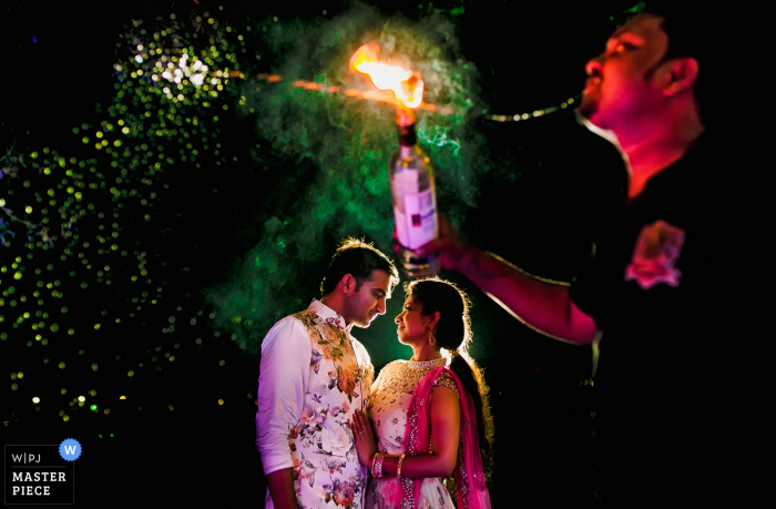 El fotógrafo de bodas de la India capturó esta imagen de una novia y un novio mirándose amorosamente mientras un respirador de fuego se presenta en primer plano.