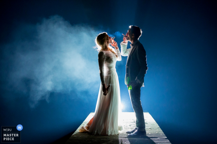 Holland wedding photographer captured this picture of a bride and groom smoking on a platform with a spotlight behind them