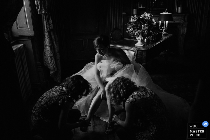 This black and white photograph of a bride getting assistance putting on her shoes while in her wedding gown was captured by a Lyon wedding photographer