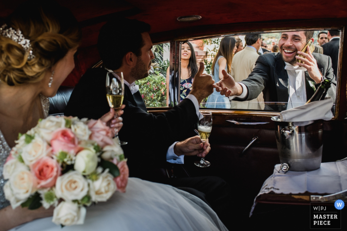 Le photographe de mariage de Cabo San Lucas a capturé cette photo d'une jeune mariée buvant du champagne dans la voiture tout en saluant les invités du mariage à travers une fenêtre ouverte