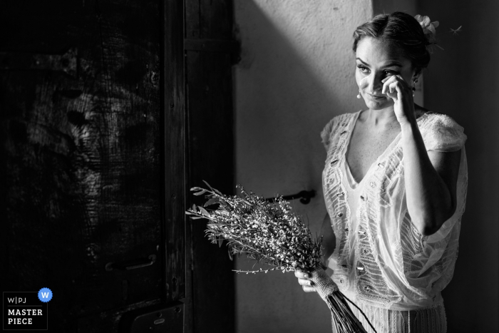 Arezzo wedding photographer captured this black and white image of a bride wiping a tear form her eye while holding her bouquet 