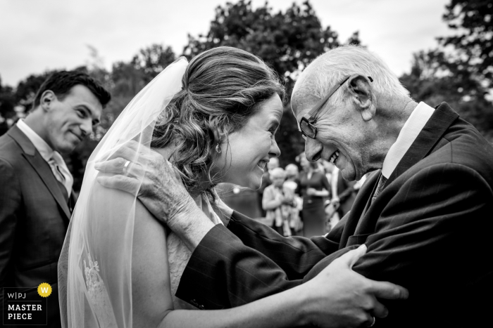 Overjissel, fotógrafo de bodas, capturó esta imagen en blanco y negro de la novia sonriendo alegremente a su padre mientras su novio sonríe.