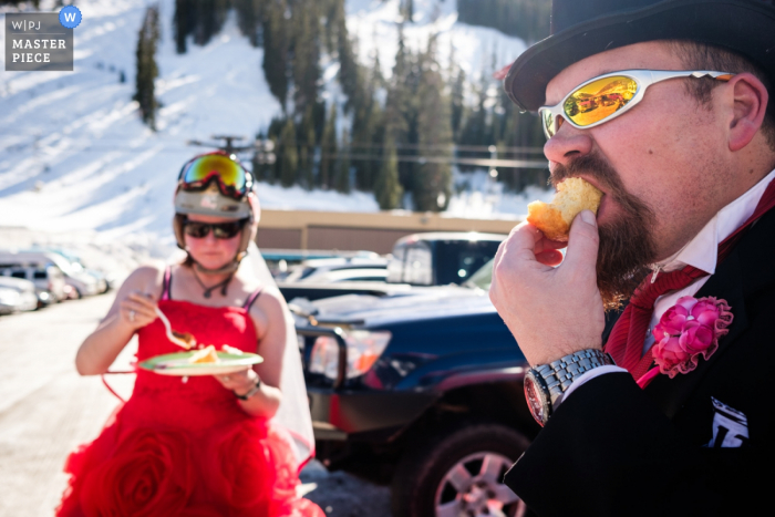 Montana wedding photographer captured this humorous photo of a bride and groom enjoying cake in ski gear in front of snow covered mountains