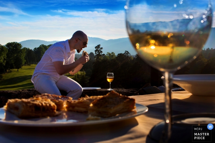 Madrid wedding photographer captured this artistic picture of a full wine glass and a sandwich, while a mountain range is magnified by the liquid in the glass and a wedding guest enjoys a sandwich in the background