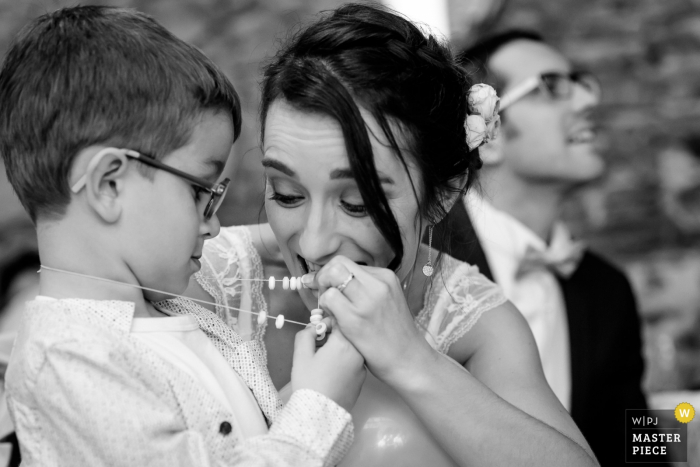 Nantes wedding photographer created this black and white picture of a bride counting the beads on the ring bearers necklace while smiling