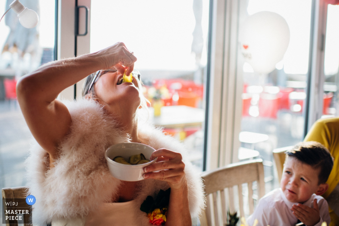 This bright photo of a bride playfully dropping food into her mouth while a little boy watches was captured by a London wedding photographer