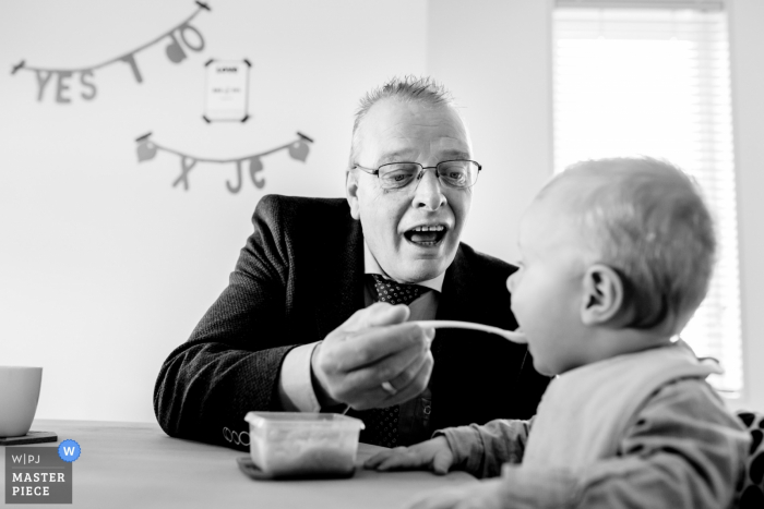 Trouwfotograaf van Overjissel creëerde deze zwart-witfoto van een bruiloftgast die zijn jonge zoon voedt met een lepel