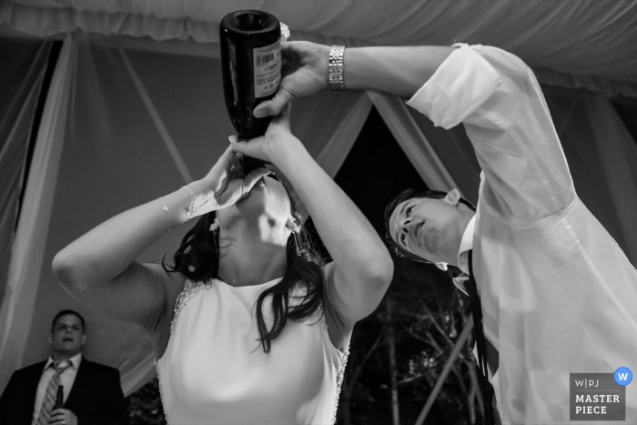 Il fotografo di matrimoni di San Diego ha catturato questa immagine umoristica in bianco e nero della sposa che beve dalla bottiglia di champagne mentre lo sposo aiuta