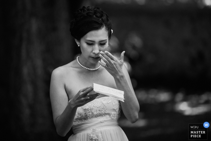 Lyon wedding photographer captured this black and white photo of a bride reading her speech from a piece of a paper as she wipes a tear from her cheek