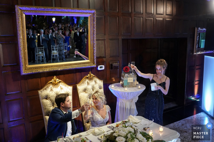 Bronx wedding photographer captured this photo of a bride and groom toasting in front of a wood paneled wall while listening to speeches from the bridal party