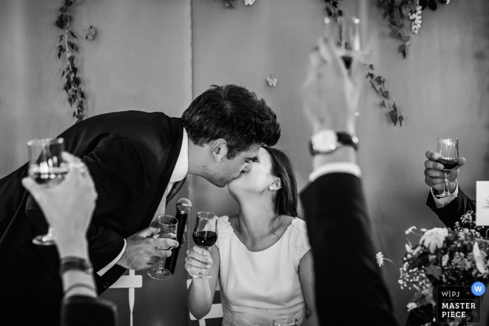 Photo by: <a href="https://www.wpja.com/contests/2017-tri2-photography-competition/toastingspeeches/2024546">William Lambelet - France</a> This black and white photo of a groom tenderly kissing the bride as onlookers raise their glasses in celebration was captured by a Montpellier wedding photographer
