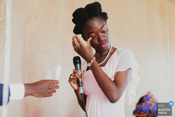 San Francisco wedding photographer captured this emotional image of the maid of honor wiping a tear while giving her speech while a hand holds out a tissue in support 