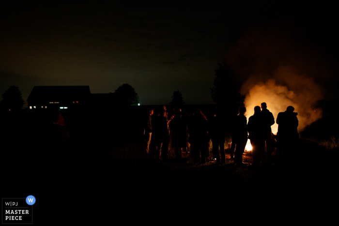 Foto von: <a href="https://www.wpja.com/contests/2017-tri2-photography-competition/fire/2049271"> Jacqueline Dersjant - Niederlande </a> Der Hochzeitsfotograf von Noord hat die Silhouetten der Hochzeitsgäste festgehalten, die nachts vor einem Lagerfeuer stehen