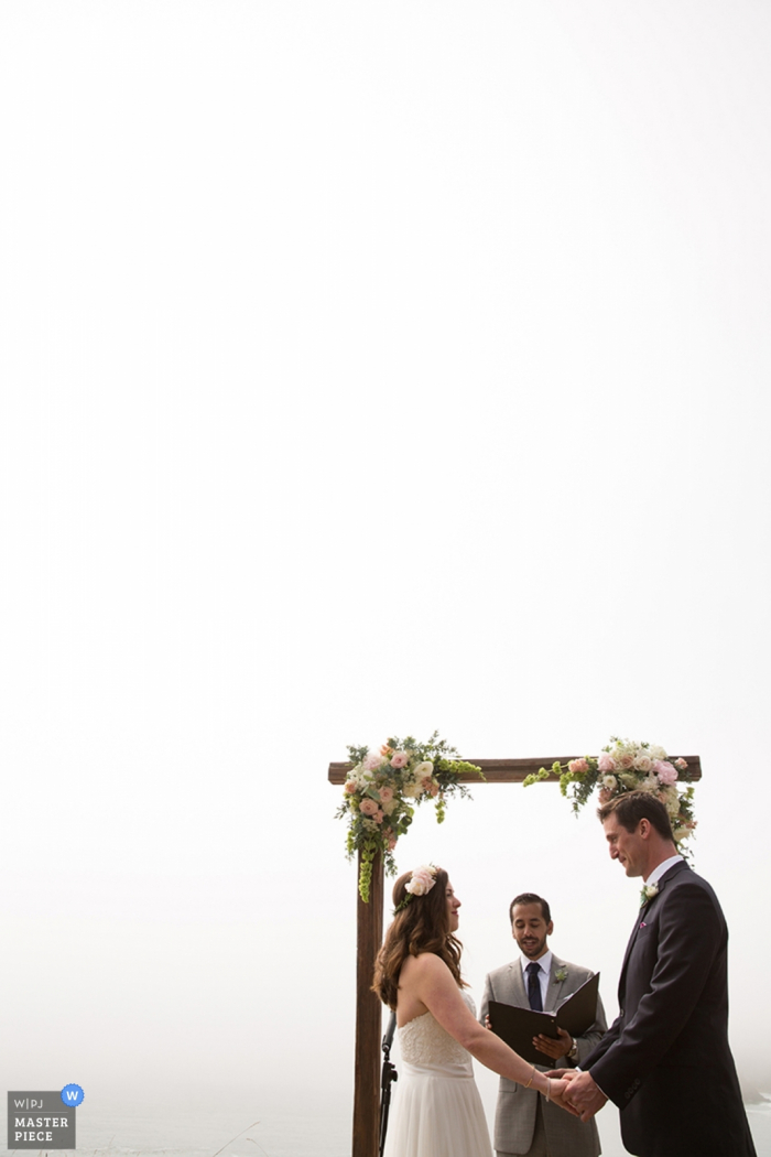 Photo by: <a href="https://www.wpja.com/contests/2017-tri2-photography-competition/minimalism/2043346">Joyce Perlman - United States</a> San Fransisco wedding photographer capture this image of a wedding ceremony being held under an flower adorned wooden arch under an overcast sky