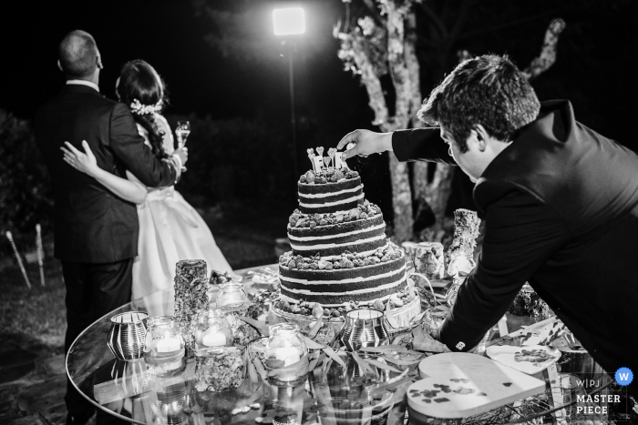 De huwelijksfotograaf van Libson maakte deze zwart-witfoto van de finishing touch die aan de taart wordt toegevoegd terwijl het gelukkige paar poseert voor foto's