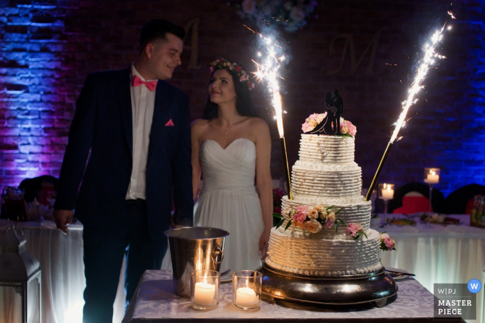 Il fotografo di matrimoni documentario Krakow Malopolskie ha realizzato questa foto della sposa e dello sposo in piedi accanto alla loro torta con stelle filanti / fuochi d'artificio.