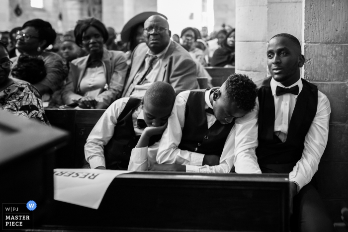 Seine-et-Marne wedding photographer captured this black and white image of two young groomsmen asleep on anothers shoulder during the church ceremony